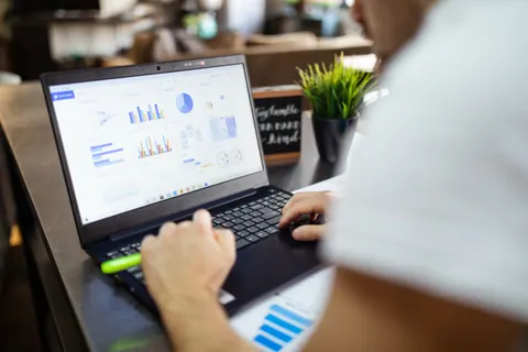 Person studying charts on a laptop beside printed graphs