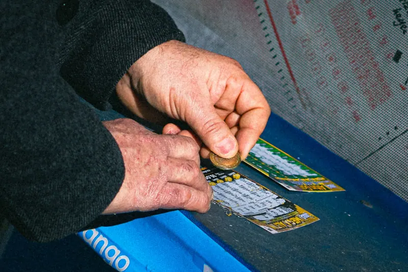 Hands using a coin to scratch off a lottery ticket on a blue table
