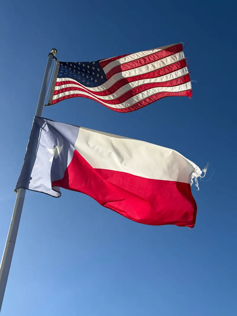 American and Texas flags waving together under a clear blue sky